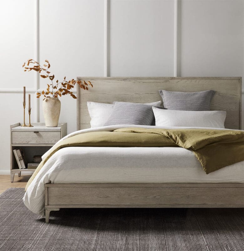 Cozy modern bedroom with light wood furniture, white linens, and a dark textured rug.