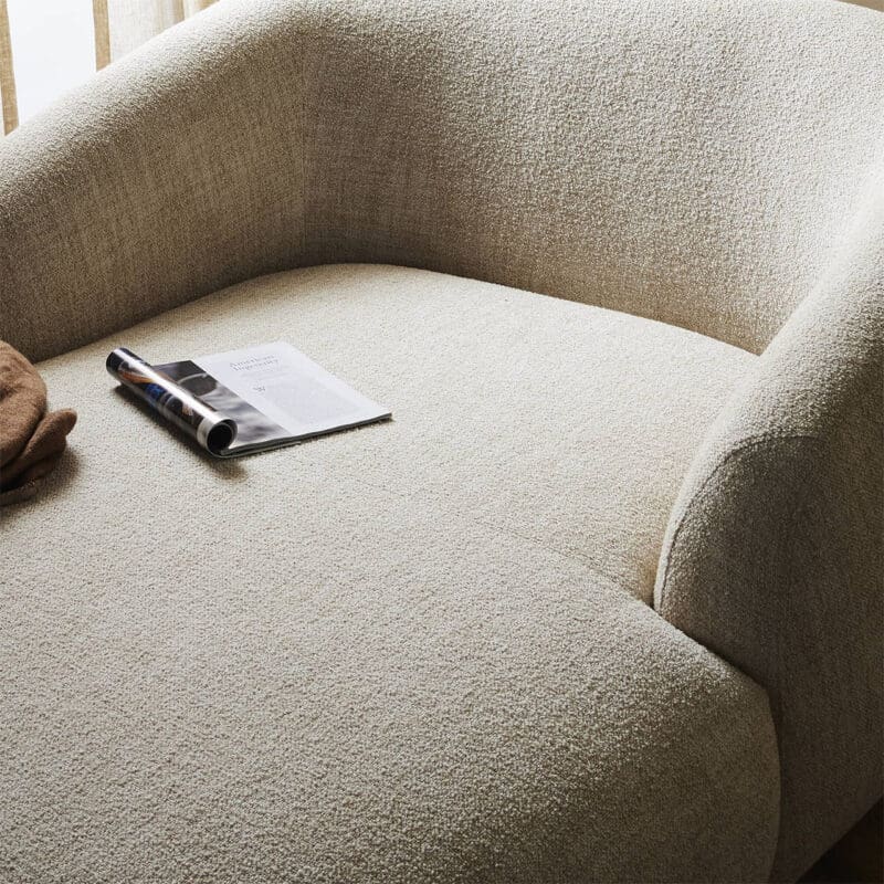 Stylish beige armchair with magazine and throw blanket creates a cozy relaxation corner.