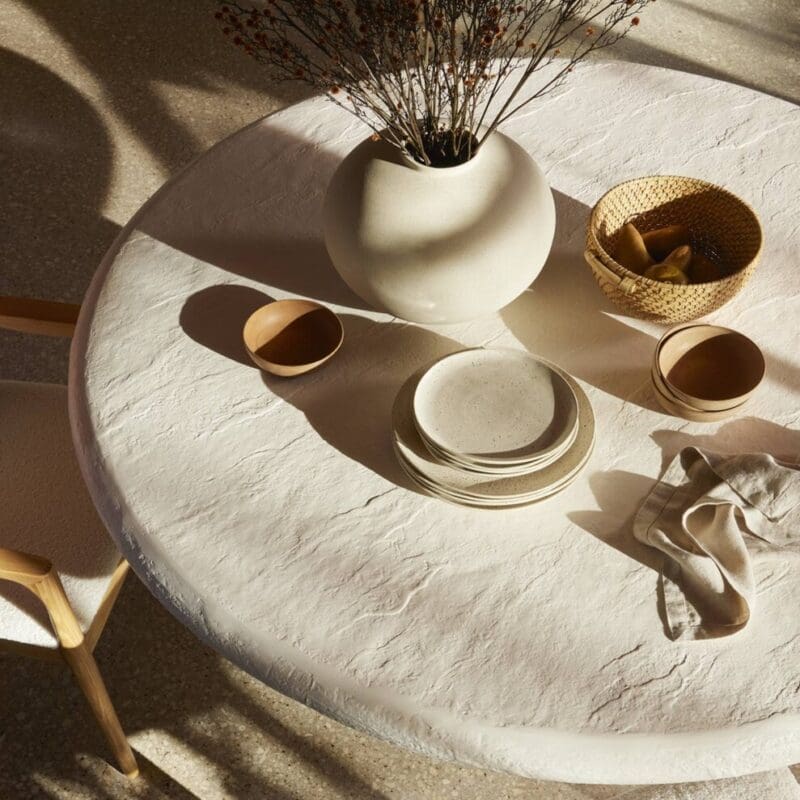 Elegant minimalist tabletop with textured white table, clay vase, dried flowers, and warm light.