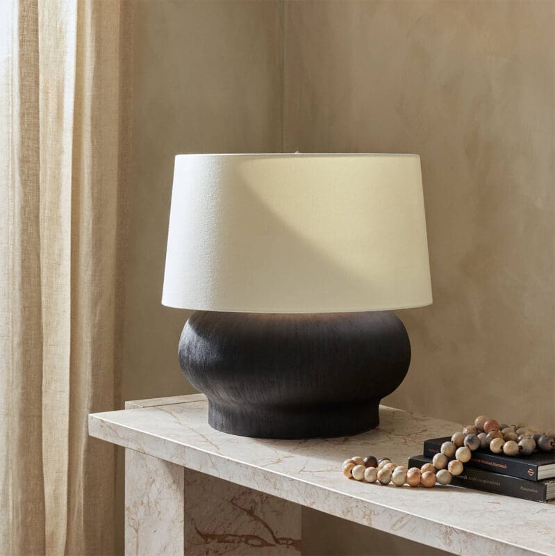 Modern lamp with dark base, white shade, wooden beads, and books in a cozy setting.