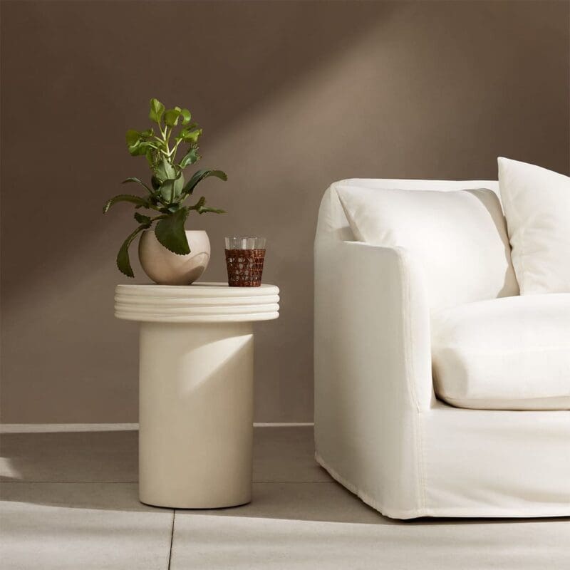 Elegant minimalist living room with a cozy white sofa, unique side table, and green plant.