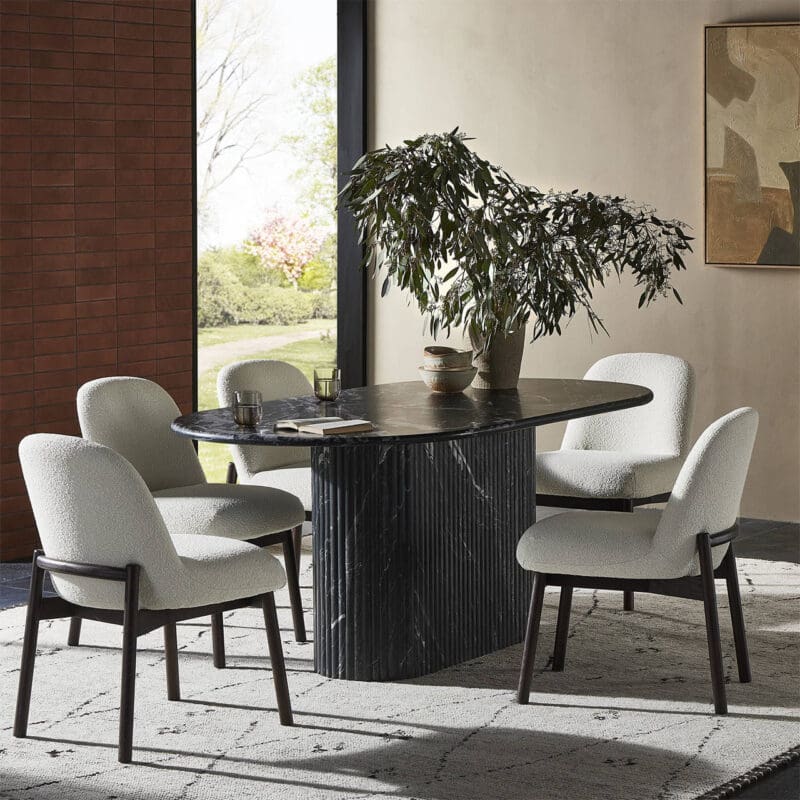 Stylish modern dining area with oval stone table, plush chairs, and vibrant garden view.