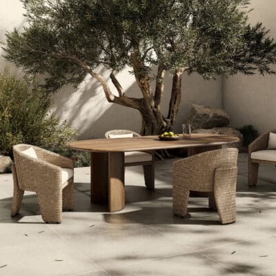 Elegant outdoor dining under an olive tree, featuring a wooden table and woven chairs.