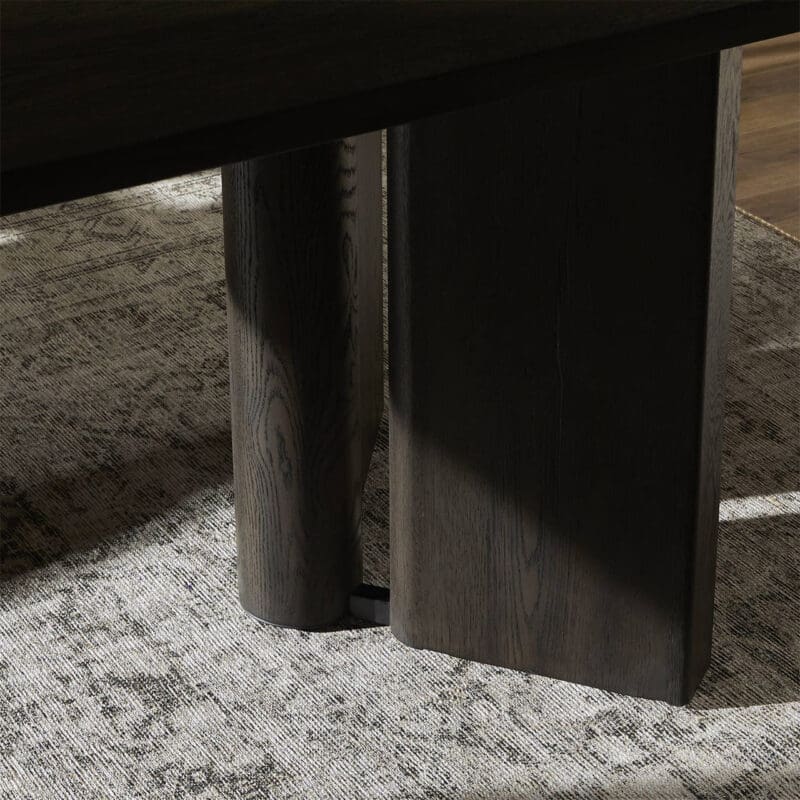Elegant wooden table leg with rich grain, softly lit against a textured neutral rug.