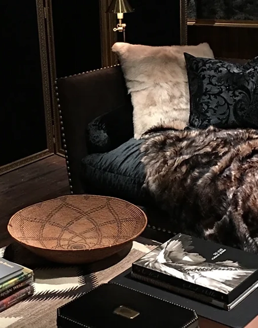Cozy living room featuring a plush black sofa, wooden bowl, and stacked coffee table books.