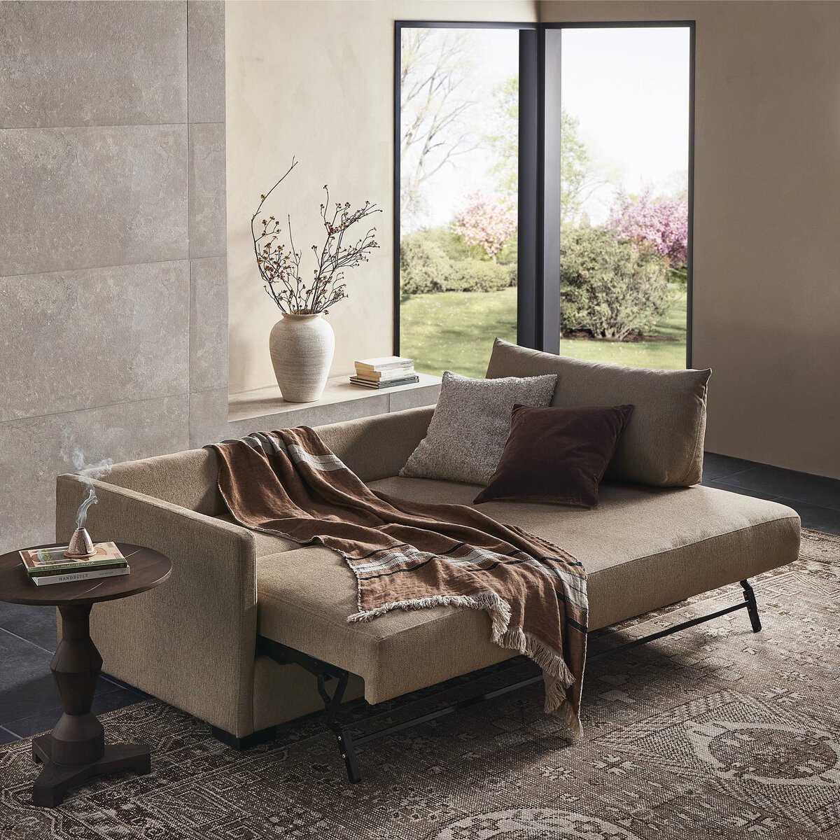 Modern cozy living room with beige asymmetric sofa, large windows, and inviting outdoor views.