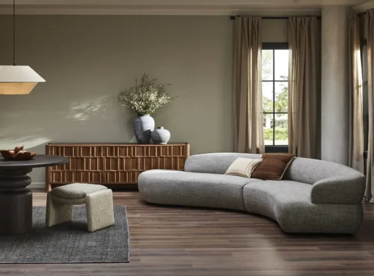 Modern living room with curved gray sofa, round dining table, and inviting natural light.