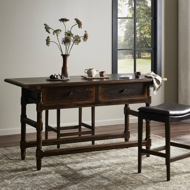 Elegant wooden table with teapot and flowers in a sunlit, serene interior space.